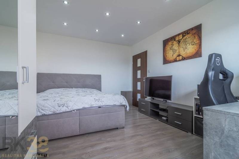 Ložnice v třípokojovém bytě s postelí, televizorem a mapou na stěně.