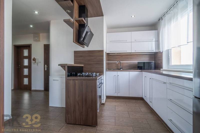 Kuchyně ve 3-pokojovém bytě s bílými skříňkami a dřevěnými doplňky.