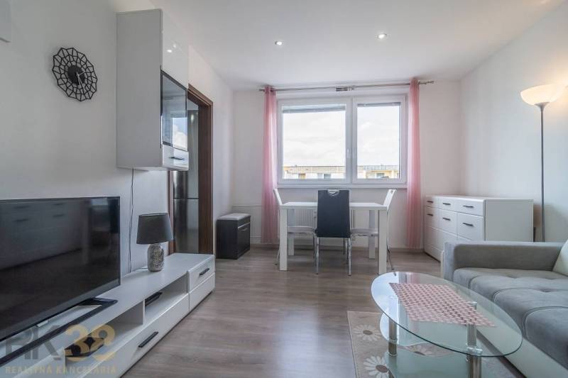 Světlý obývací pokoj se stolem, televizí a sedačkou v 3-pokojovém bytě.