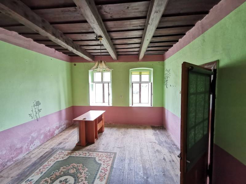 Pokoj v rodinném domě s dřevěným stropem, starým stolem a kobercem.