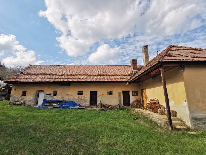 Starší rodinný dům v Nitrianskych Sučanoch obklopený trávou a dřevem na ulici Nitrianske Sučany.