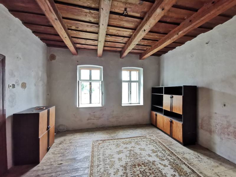 Pokoj v rodinném domě s dřevěným stropem, okna, skříňky, koberec na podlaze.