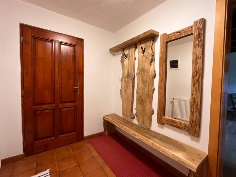 Dřevěná lavička a věšák s přírodním zrcadlem v interiéru rodinného domu.