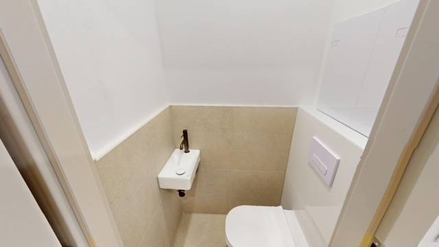 Kompaktní WC s umyvadlem v 2pokojovém bytě, béžové dlaždice a bílá stěna.