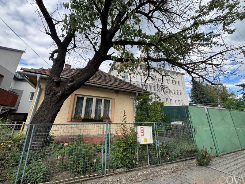 Rodinný dům v Ilavě s oplocenou zahradou, stromem a sousedními budovami v pozadí.