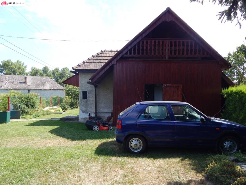 Auto zaparkované u chaty v Klížské Němé, obklopené zeleným trávníkem a stromy.