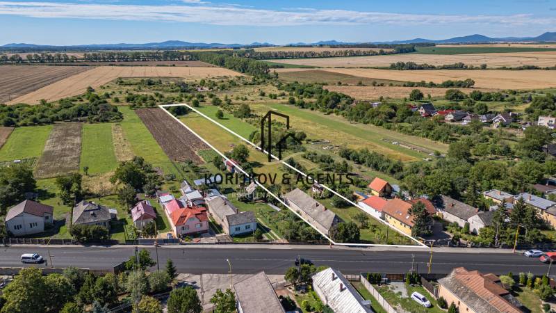 Pozemky k bydlení v Sečovcích, zelená pole, několik domů a velká cesta vpředu.