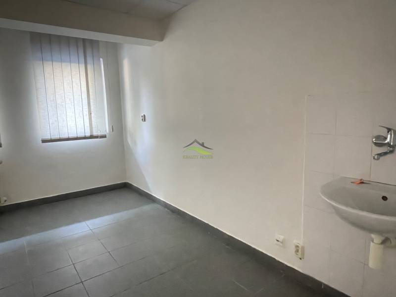 Místnost v kanceláři s podlahou z dlaždic, okno se žaluzií a umyvadlo.