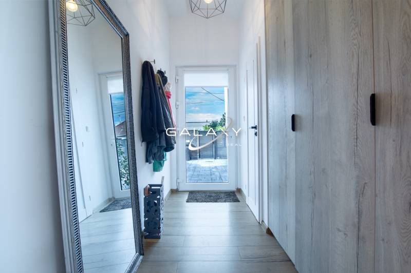 Chodba v rodinném domě s velkým zrcadlem, věšáky a skříní.