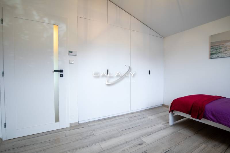 Ložnice v rodinném domě s bílou skříní, dveřmi a postelí s barevnou přikrývkou.