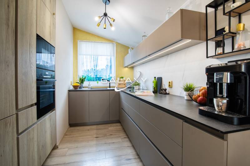 Kuchyně v rodinném domě s moderními skříňkami, spotřebiči a světlým oknem.