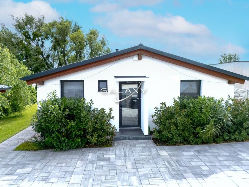 Rodinný dům v Černé Vodě s bílou fasádou, obklopený zelení a dlažbou.