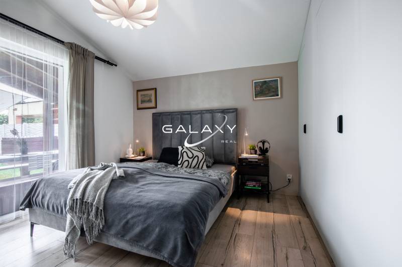 Ložnice v rodinném domě s postelí, nočními stolky a lampami, s výhledem ven.