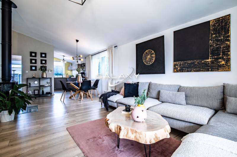 Obývací pokoj v rodinném domě s šedou sedačkou, dřevěným stolem a jídelním koutem.