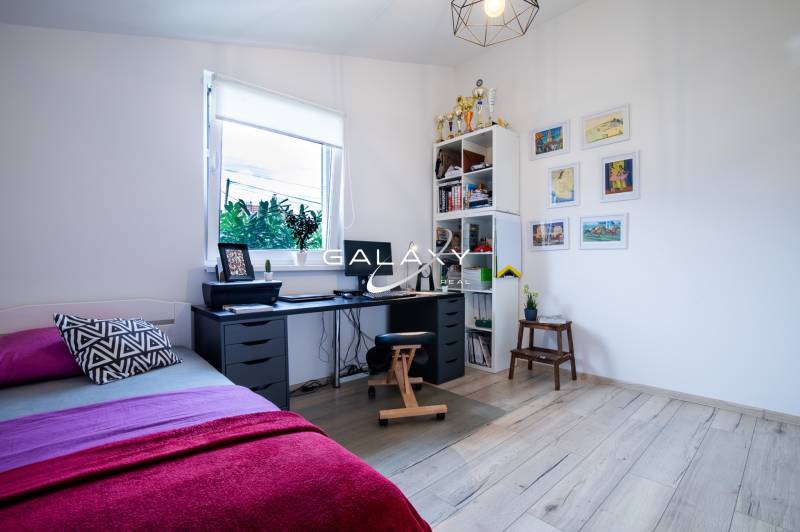 Pracovní kout v rodinném domě se stolem, postelí a policí s trofejemi.