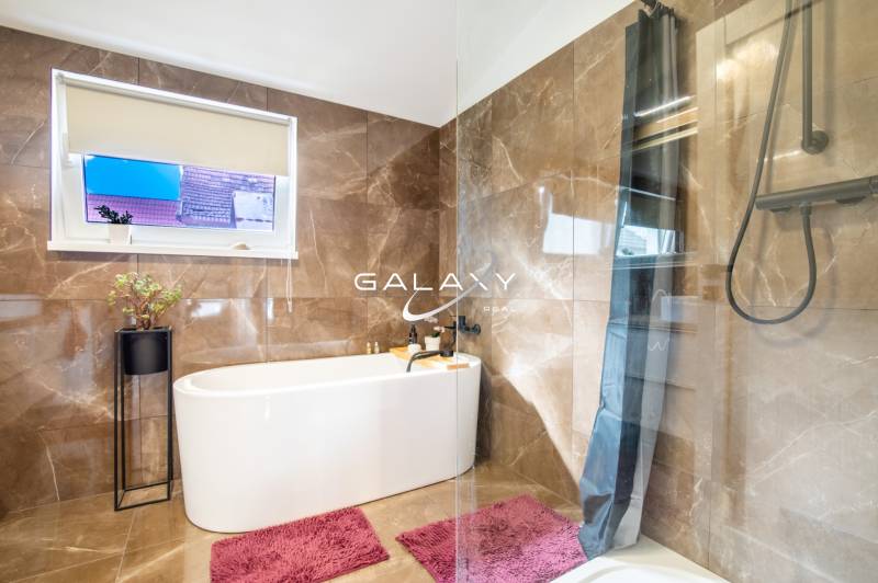 Koupelna v rodinném domě s vanou, mramorovými obklady a růžovými koberci.