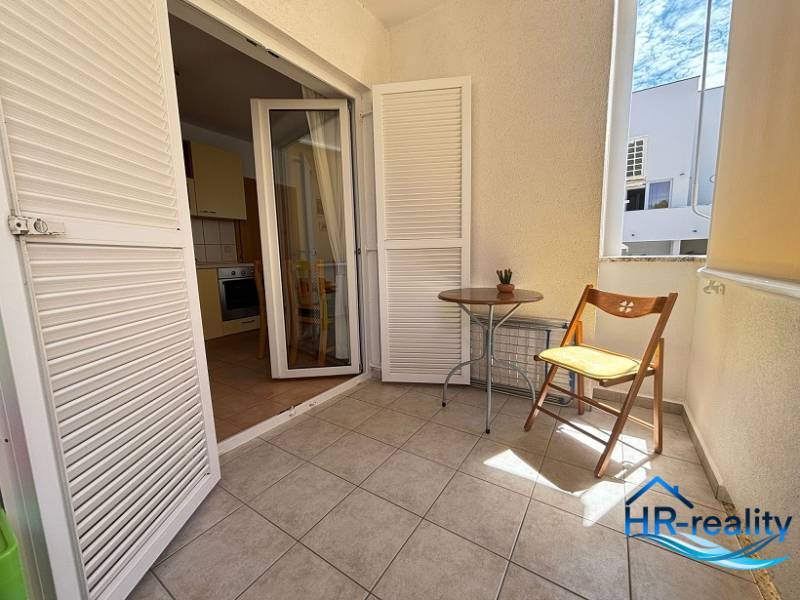 Balkon ve 2-pokojovém bytě s bílými žaluziemi a dřevěnou židlí.