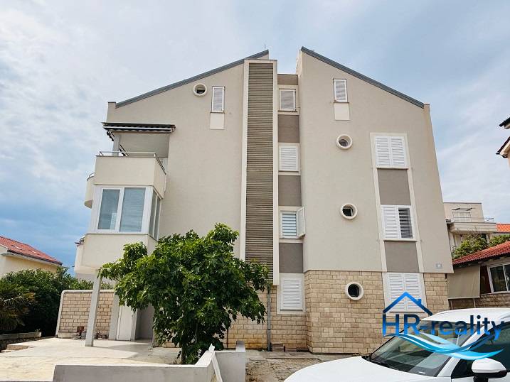 Exteriér budovy v Novalji s 3-pokojovým bytem, bílé okenice a balkón.