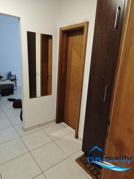 Chodba s dlaždicovou podlahou, zrcadlem a dřevěnými dveřmi v 2pokojovém bytě.