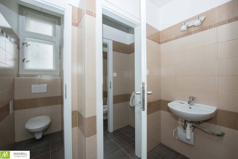 Koupelna v kancelářích s béžovými obklady a umyvadlem.