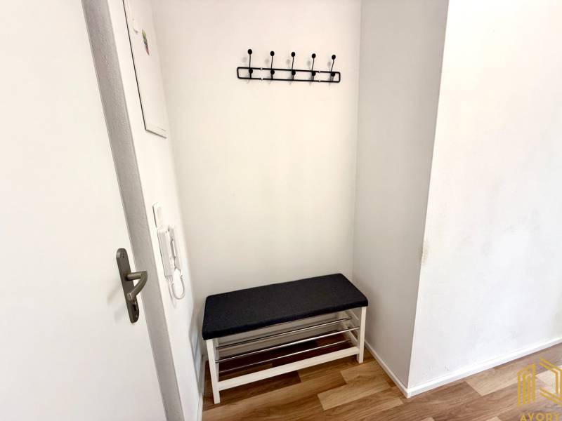 Vstupní chodba v 2-pokojovém bytě s lavicí a věšákem na stěně.