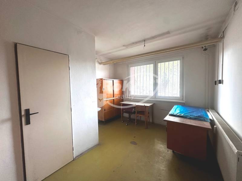 Kancelář v obchodních prostorech obsahuje stoly, židle, skříně a radiátor.
