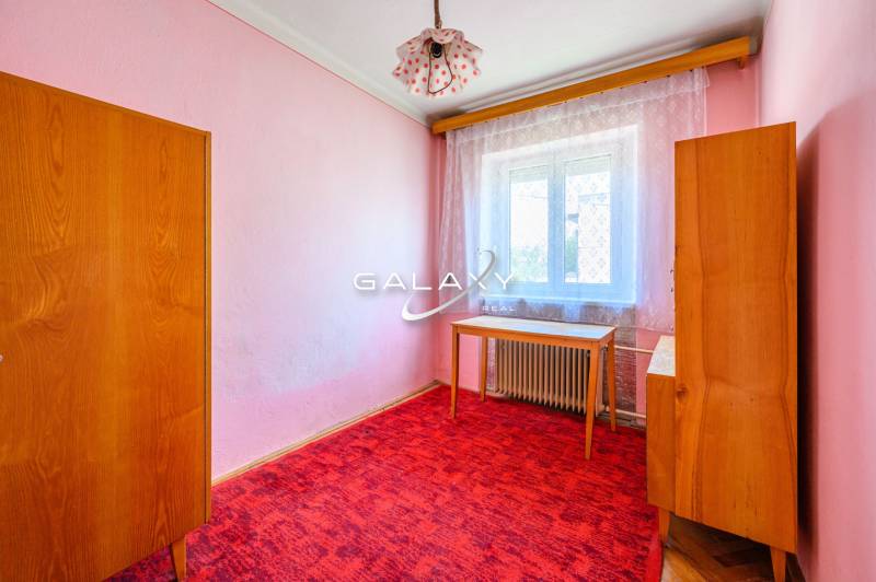 Pokoj v rodinném domě s růžovými stěnami, nábytkem a červeným kobercem.