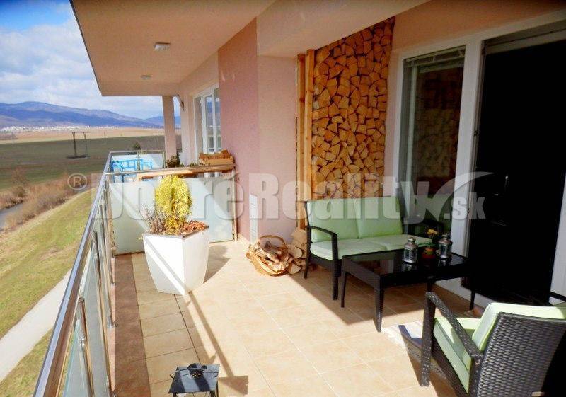 Balkon 2pokojového bytu s výhledem na přírodu, pohodlným sezením a dekorativním dřevem.
