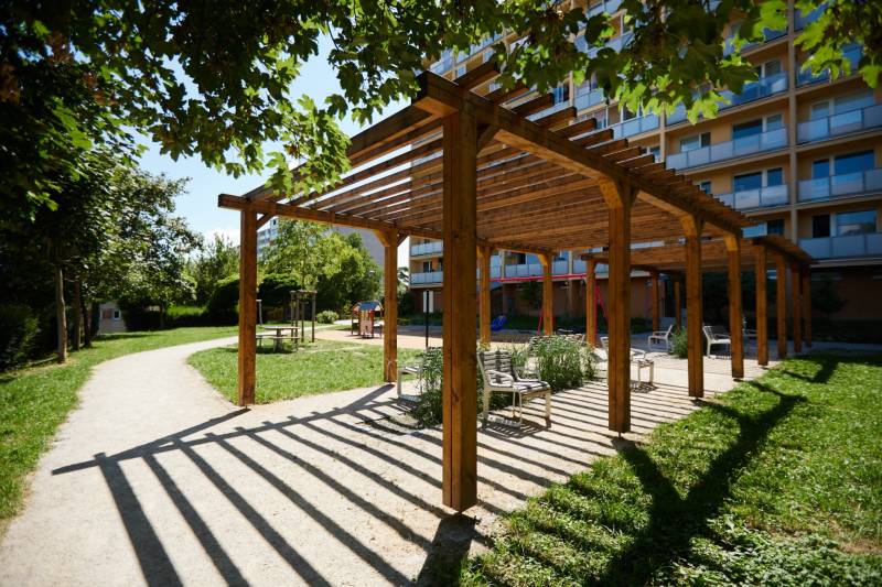 Dřevěná pergola s lavičkami v parku v Košicích, městská část Jih, obklopená zelení.