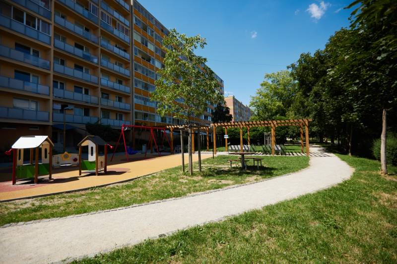 Hřiště s bytovým domem v Košicích - městské části Jih, obklopené zelení a chodníkem.