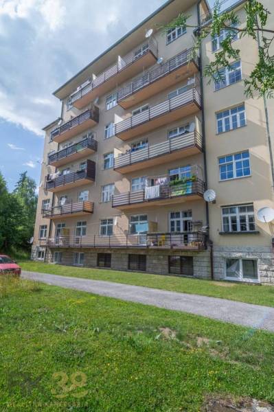 Pětipatrový bytový dům ve Vysokých Tatrách s balkony a zeleným trávníkem.