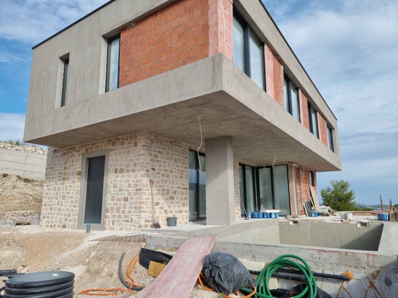 Rozestavěná vila ve Vodicích s betonovou a cihlovou fasádou, bazénem a verandou.