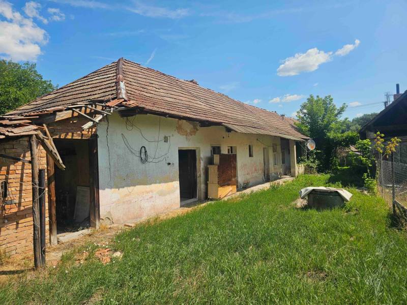 Rodinný dům v Hronovcích s opuštěnou fasádou, starší střechou a travnatým okolím.