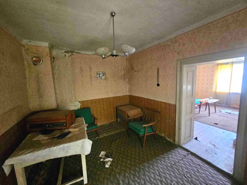 Obývací pokoj v rodinném domě s retro nábytkem a poškozenými stěnami.