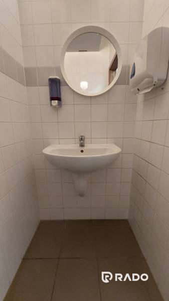 Bílé obkladačky a umyvadlo s kulatým zrcadlem v kanceláři.