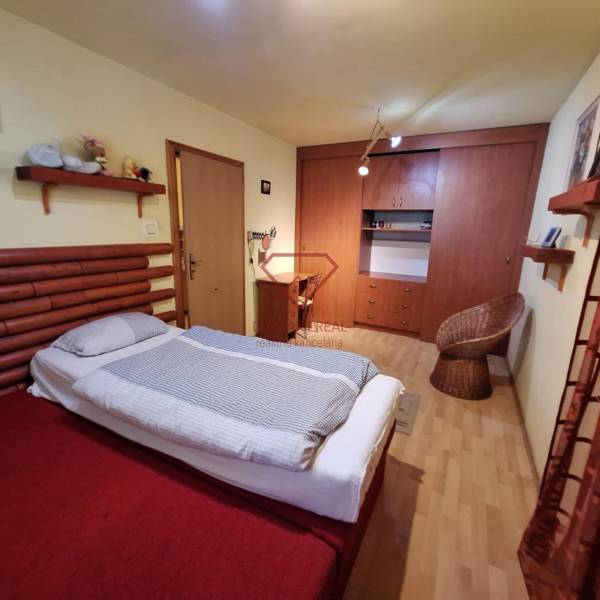 Ložnice rodinného domu s postelí, skříní a ratanovým křeslem.