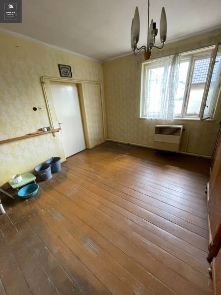 Interiér rodinného domu s dřevěnou podlahou, starším nábytkem a zavěšeným svítidlem.