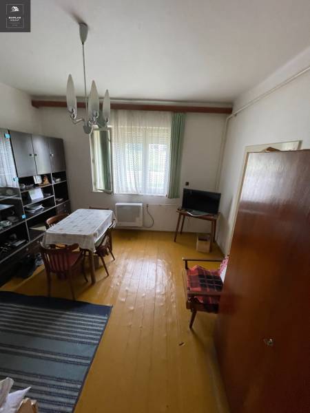 Jídelna v rodinném domě s dřevěnou podlahou, jednoduchým stolem a skříňkou na stěně.