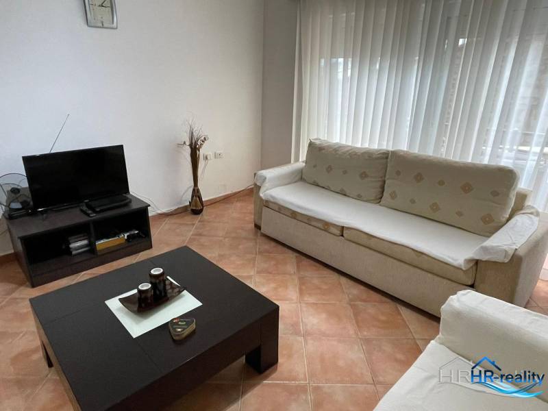 Obývací pokoj v rekreačním apartmánu s pohovkami, stolkem a televizorem.