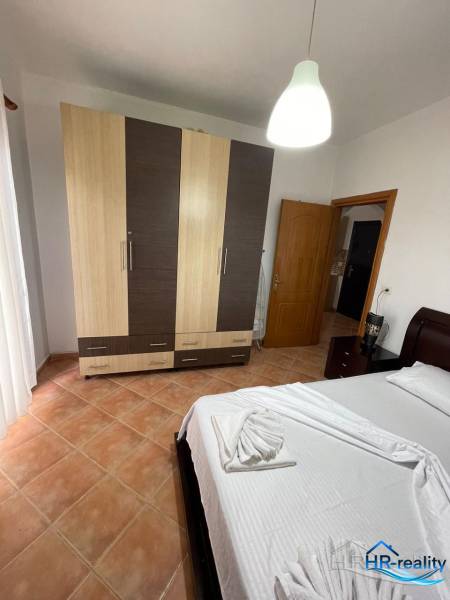 Světlá ložnice v rekreačním apartmánu s postelí, šatní skříní a dlaždicovou podlahou.
