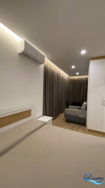 Interiér rekreačního apartmánu s postelí, pohovkou, závěsy a klimatizací.