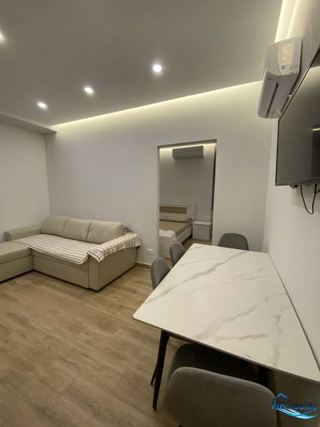 Obývací prostor rekreačního apartmánu s pohovkou, jídelním stolem a vstupem do ložnice.