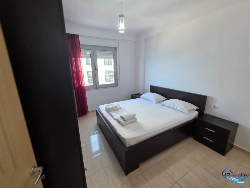 Ložnice v rekreačním apartmánu s manželskou postelí, nočními stolky a oknem s červenými závěsy.