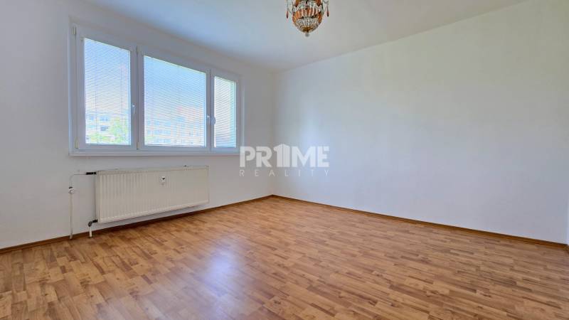 Světlý pokoj s velkým oknem, dřevěnou podlahou a radiátorem ve 3pokojovém bytě.