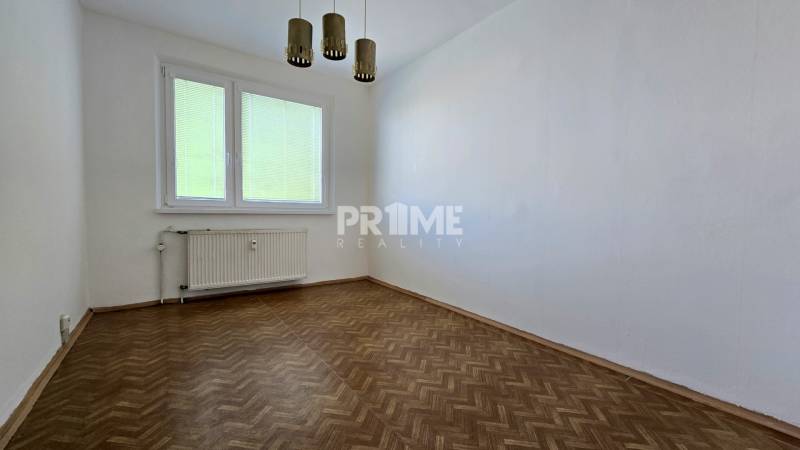 Pokoj v 3-pokojovém bytě s dřevěnou podlahou, bílými stěnami a oknem se žaluziemi.