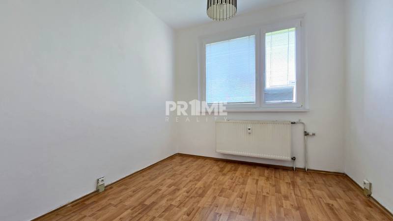 Prázdný pokoj s dřevěnou podlahou a radiátorem ve 3pokojovém bytě.