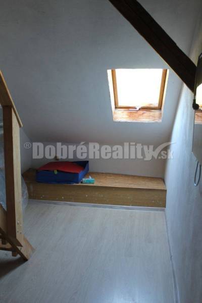 Podkrovní místnost v rodinném domě se střešním oknem a dřevěnou lavicí.
