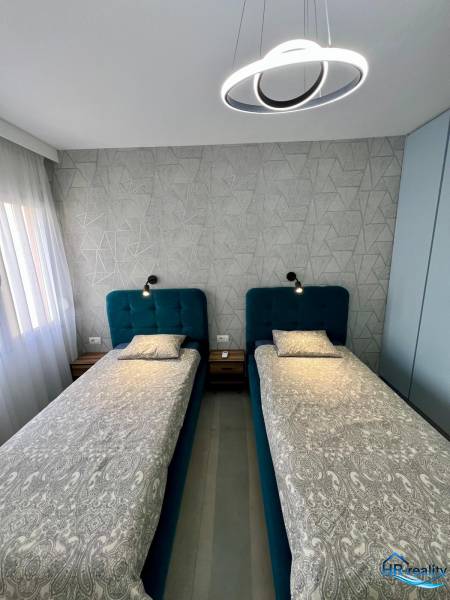 Dvoulůžková ložnice s geometrickou tapetou a moderním osvětlením v rekreačním apartmánu.