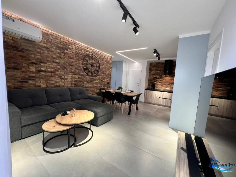 Obývací pokoj v rekreačním apartmánu s cihlovou stěnou, pohovkou a televizí.