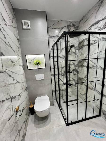 Koupelna rekreačního apartmánu s toaletou, sprchovým koutem a mramorovými obklady.